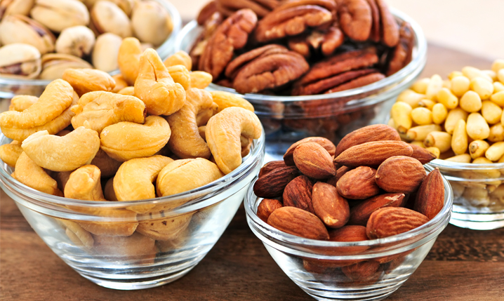 several bowls containing nuts such as peanuts, macadamia nuts, cashew nuts, and pistachios