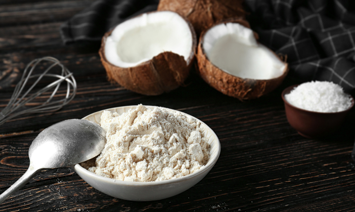 a bowl of coconut flour with opened coconuts in the background