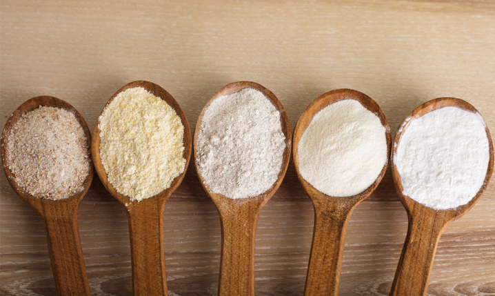five wooden spoons containing different varieties of flour