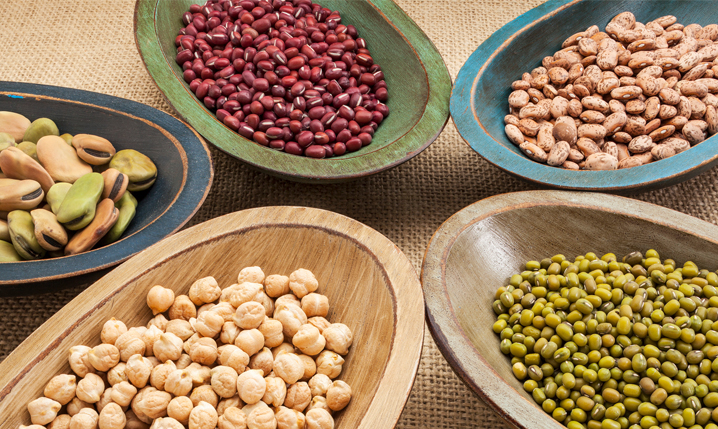 assorted beans or legumes in five separate colorful wooden bowls