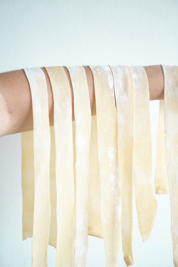 strands of raw uncooked pappardelle pasta hanging from a person's arm