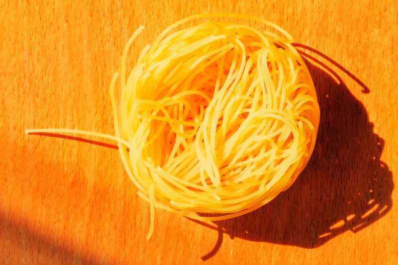 a nest of raw uncooked angel hair pasta on a chopping board shot from above